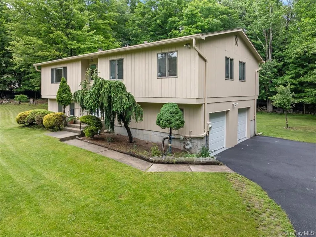 Raised ranch with a front yard, driveway, an attached garage, and view of wooded area Raised ranch with a front yard, driveway, an attached garage, and view of wooded area