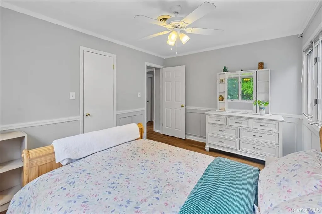 Bedroom featuring ornamental molding, dark wood-type flooring, a wainscoted wall, and a ceiling fan Bedroom featuring ornamental molding, dark wood-type flooring, a wainscoted wall, and a ceiling fan
