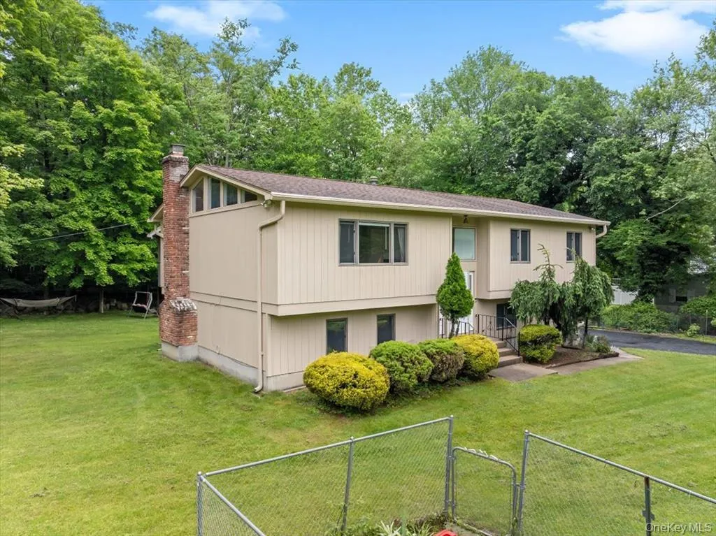 Split foyer home with a chimney, a gate, view of scattered trees, and a shingled roof Split foyer home with a chimney, a gate, view of scattered trees, and a shingled roof