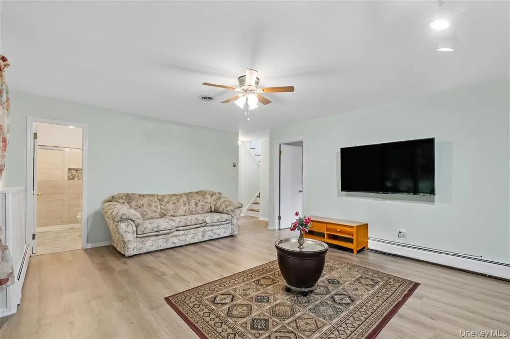 Living room featuring light wood-type flooring, stairs, a baseboard radiator, and ceiling fan Living room featuring light wood-type flooring, stairs, a baseboard radiator, and ceiling fan