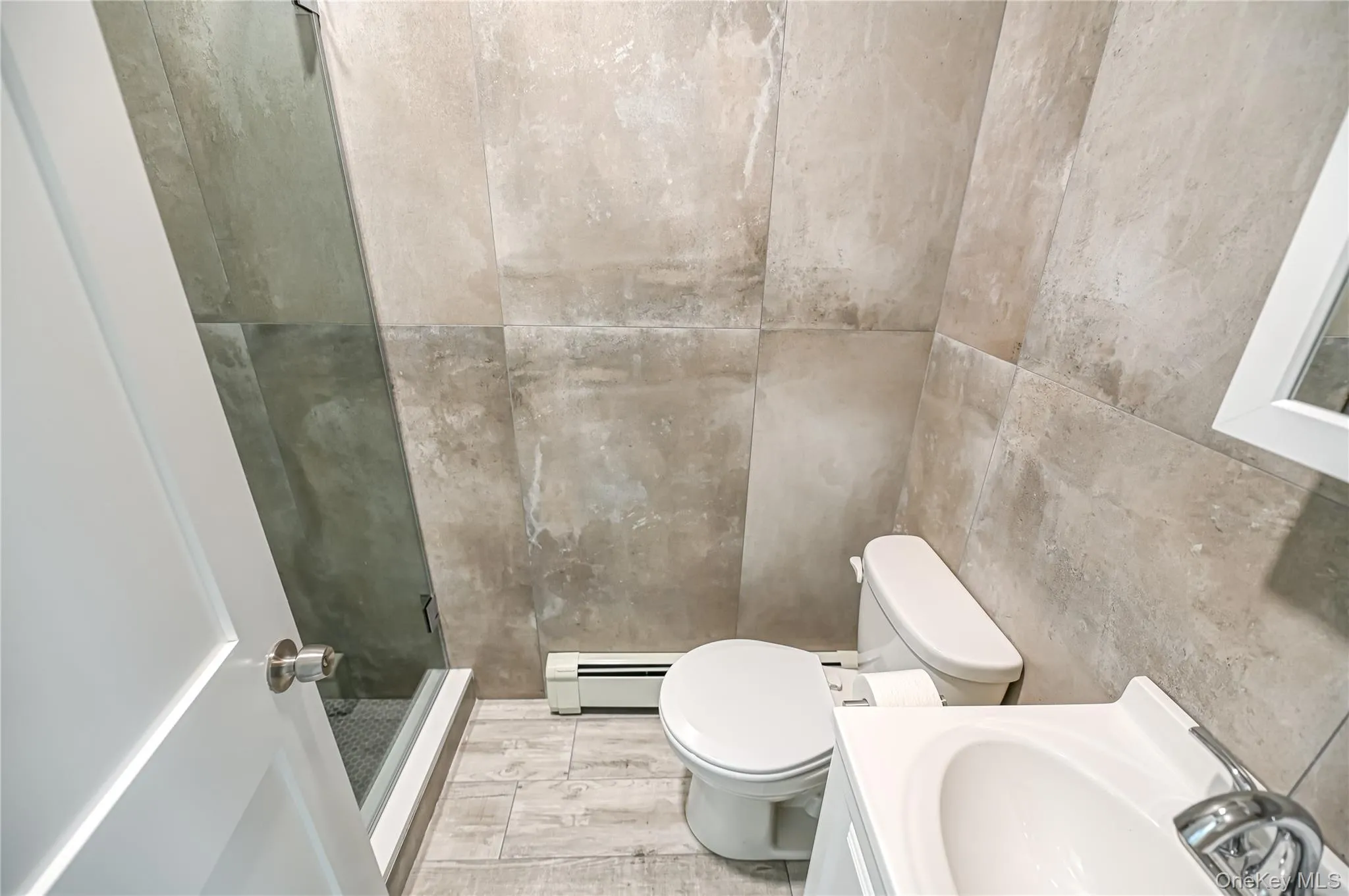 Bathroom with a shower stall, a baseboard radiator, vanity, and tile walls Bathroom with a shower stall, a baseboard radiator, vanity, and tile walls