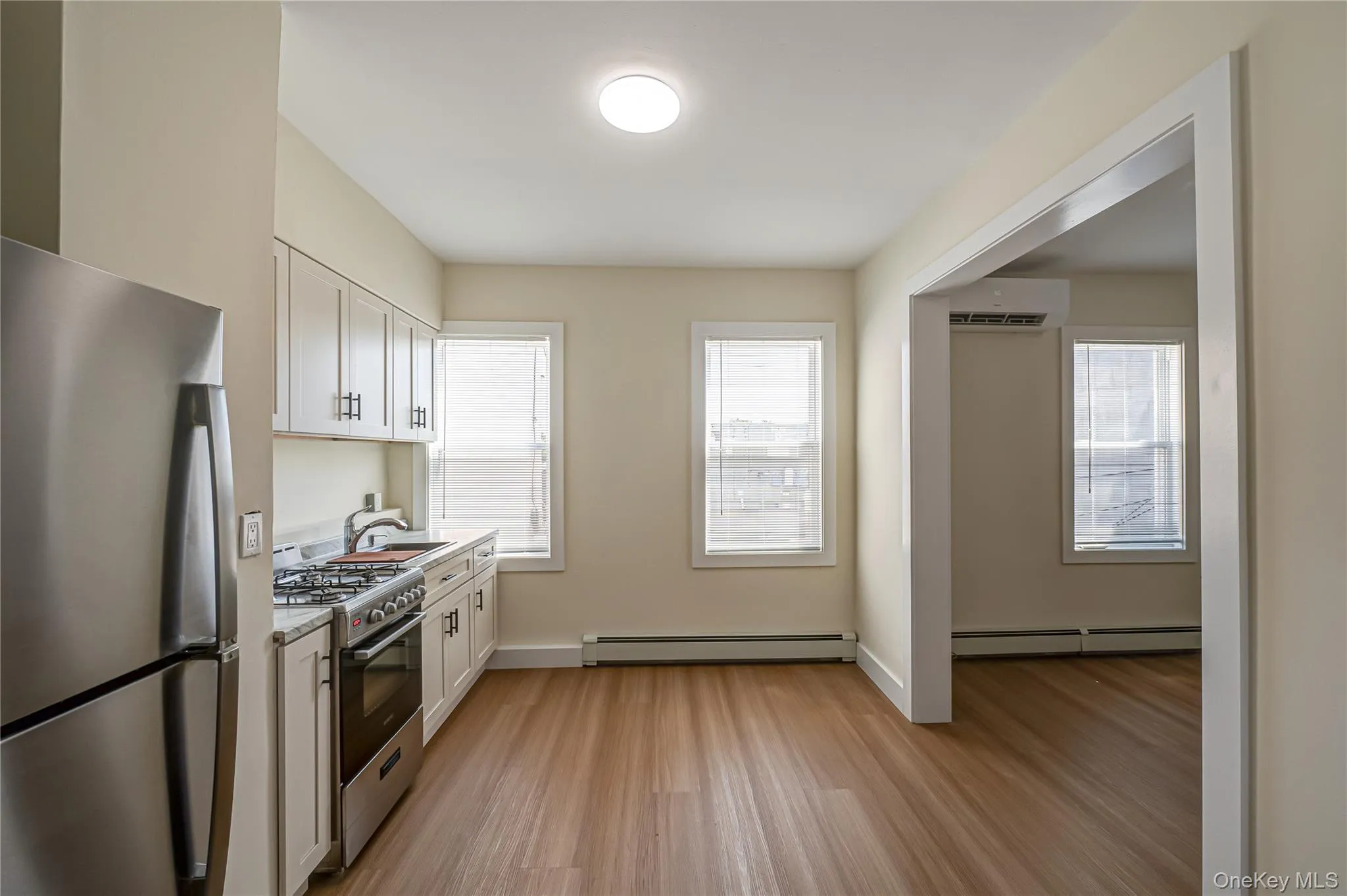 Kitchen featuring appliances with stainless steel finishes, light wood-type flooring, white cabinets, a baseboard radiator, and a wall mounted AC Kitchen featuring appliances with stainless steel finishes, light wood-type flooring, white cabinets, a baseboard radiator, and a wall mounted AC