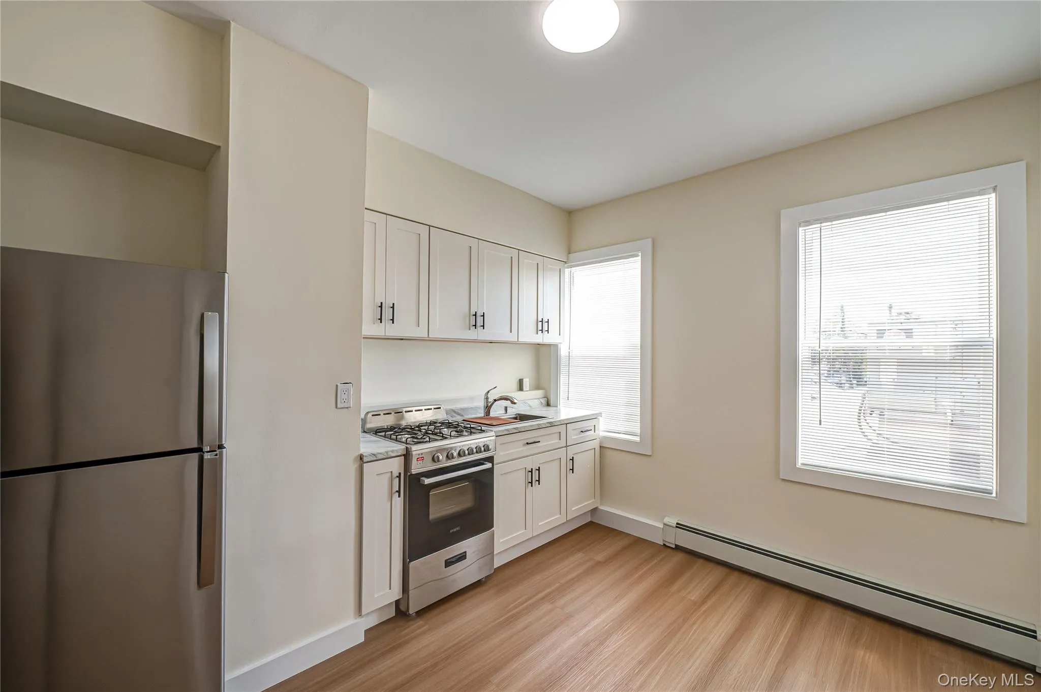 Kitchen with appliances with stainless steel finishes, a baseboard radiator, white cabinetry, and light wood finished floors Kitchen with appliances with stainless steel finishes, a baseboard radiator, white cabinetry, and light wood finished floors