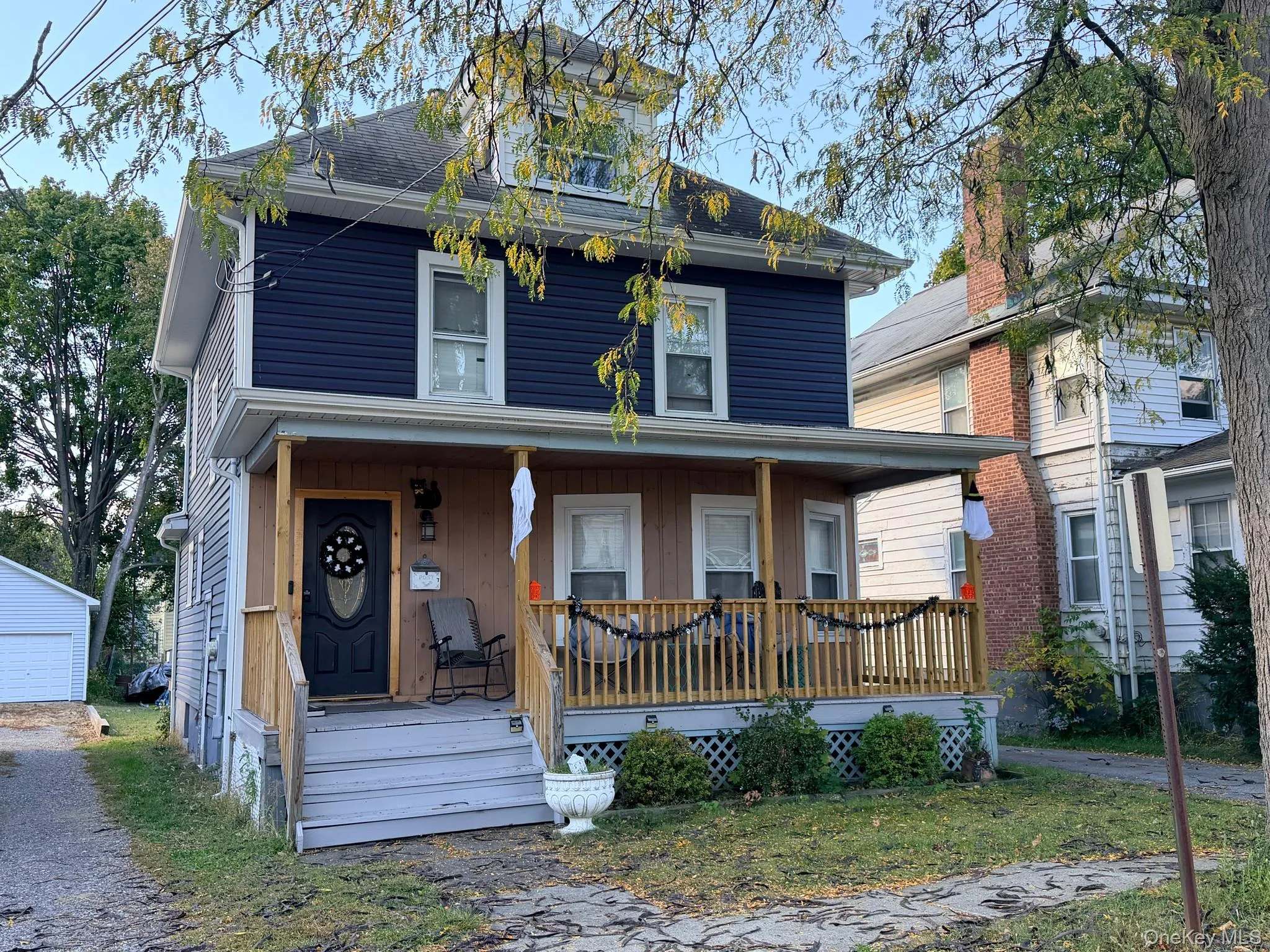 Two-story residence featuring a covered front porch with wood railings and steps, dark blue horizontal siding, and a white detached garage Two-story residence featuring a covered front porch with wood railings and steps, dark blue horizontal siding, and a white detached garage