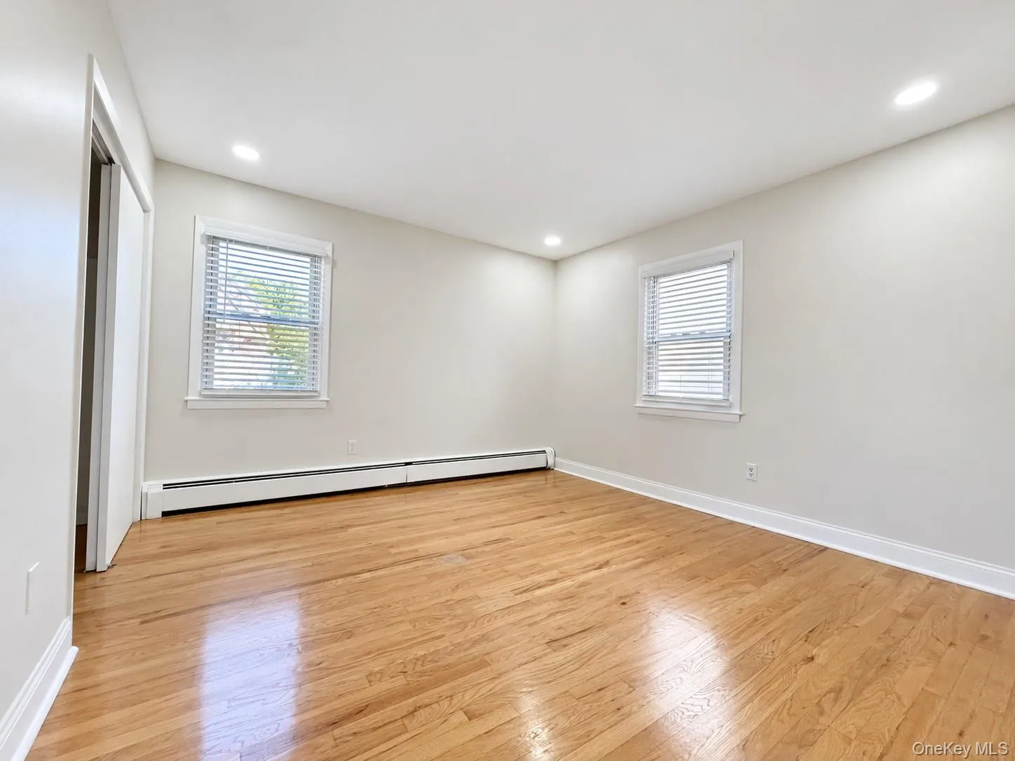 Hardwood flooring, recessed lighting, white walls, two windows with blinds, and baseboard heating Hardwood flooring, recessed lighting, white walls, two windows with blinds, and baseboard heating