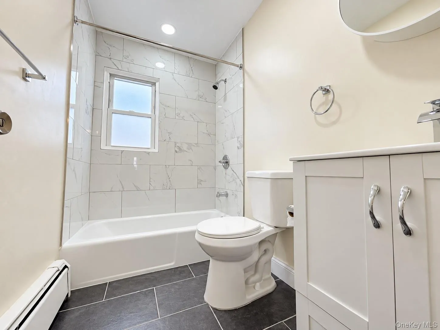 White vanity with chrome hardware, dark tile flooring, and a shower/tub combination featuring white subway tile White vanity with chrome hardware, dark tile flooring, and a shower/tub combination featuring white subway tile