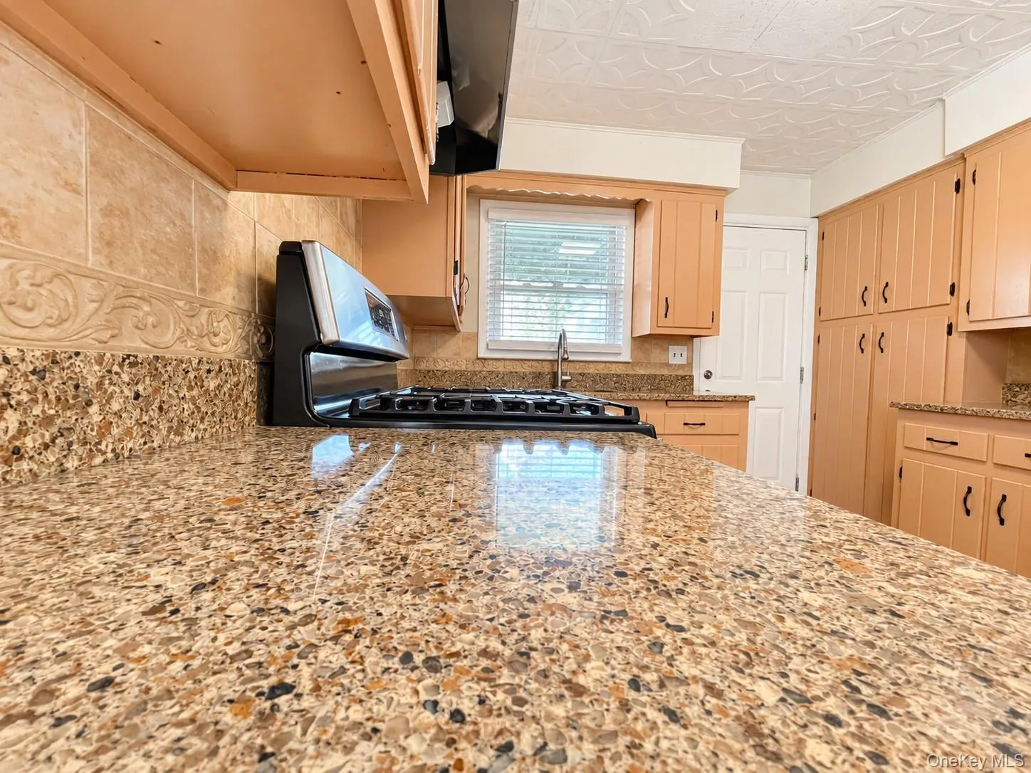 Granite-finish countertops with a tile backsplash, wood cabinetry, and a gas range Granite-finish countertops with a tile backsplash, wood cabinetry, and a gas range