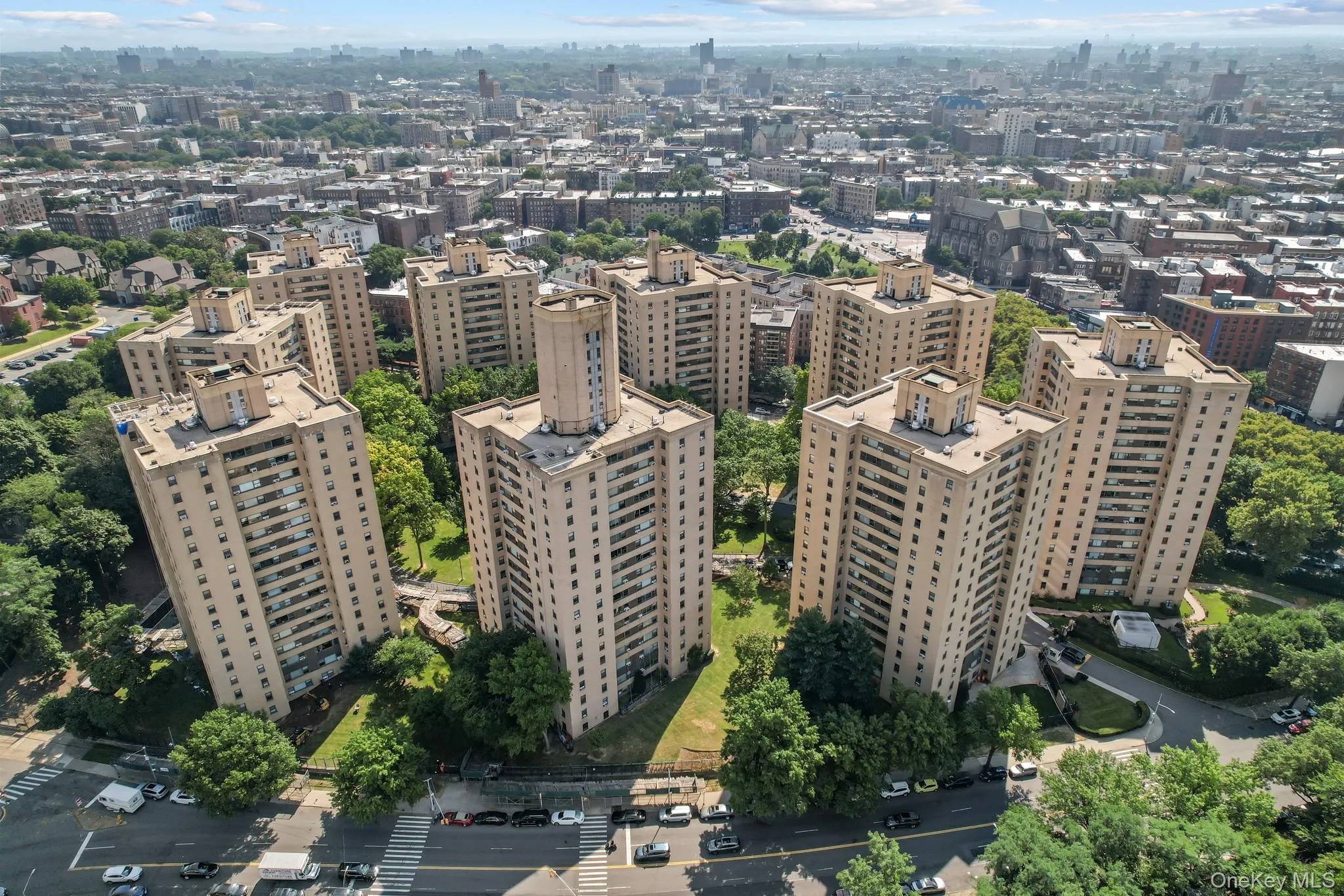 Multiple high-rise residential buildings with numerous balconies, surrounded by mature trees and paved pathways, featuring a city backdrop Multiple high-rise residential buildings with numerous balconies, surrounded by mature trees and paved pathways, featuring a city backdrop
