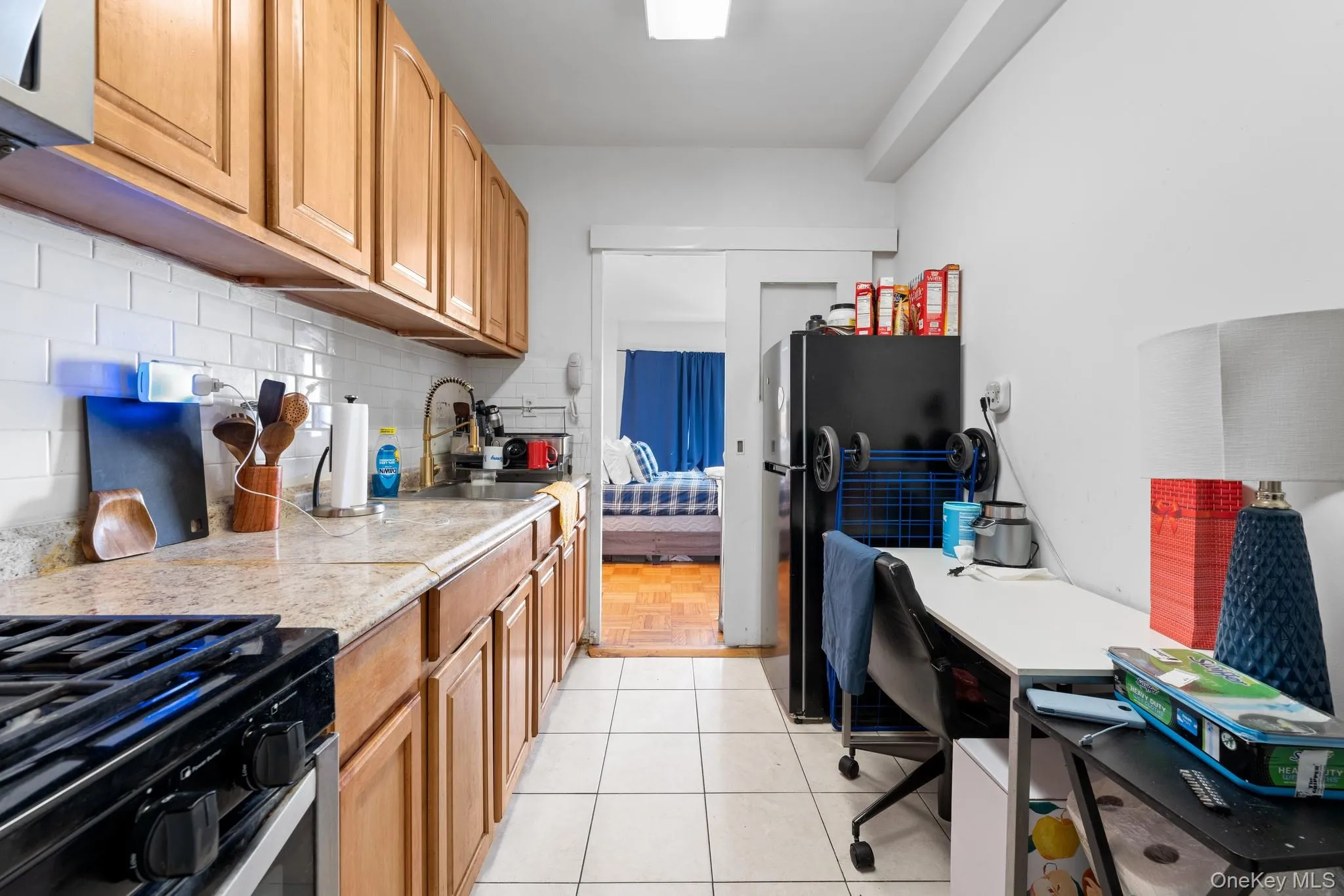 Kitchen featuring white subway tile backsplash, wood cabinetry, stone-finish countertops, and white floor tiling Kitchen featuring white subway tile backsplash, wood cabinetry, stone-finish countertops, and white floor tiling