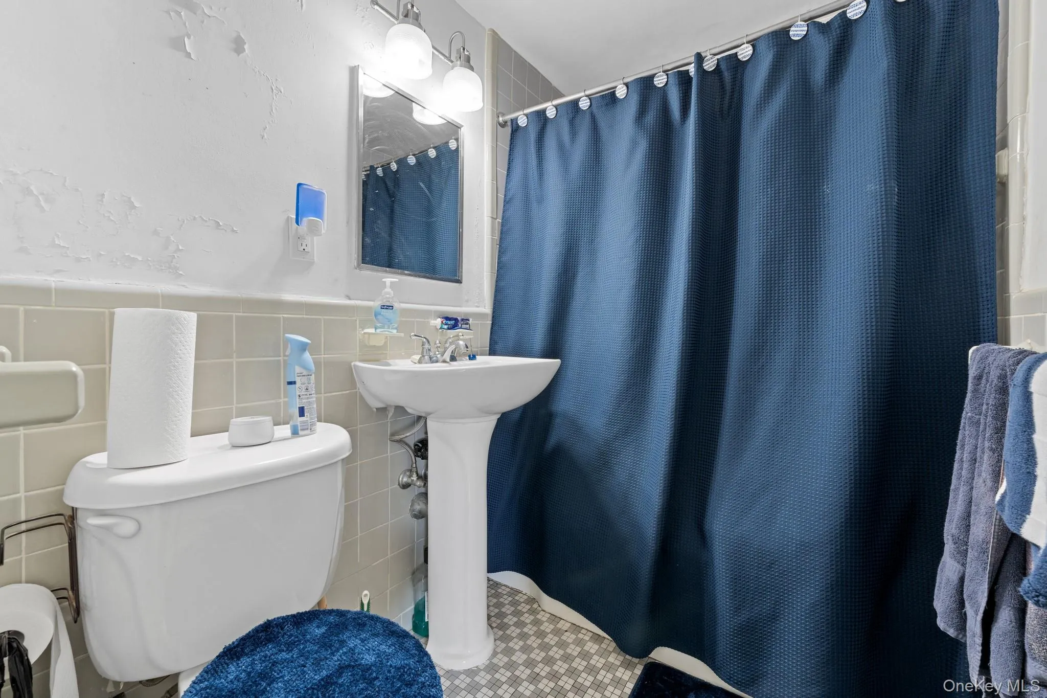 Pedestal sink, wall-mounted mirror, overhead vanity lighting, tiled flooring, and tiled wall accents Pedestal sink, wall-mounted mirror, overhead vanity lighting, tiled flooring, and tiled wall accents