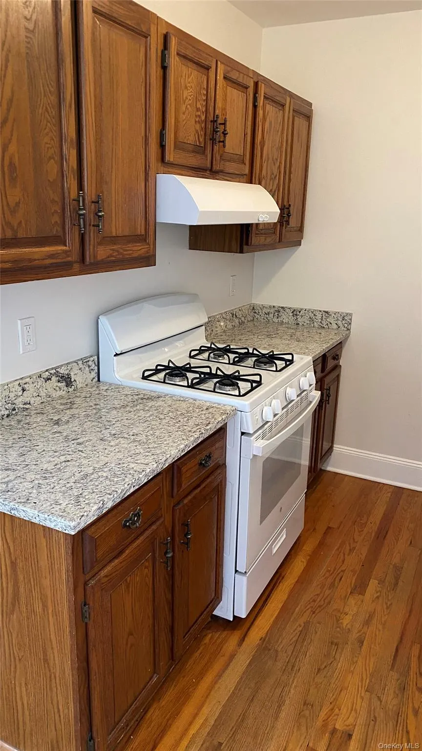 Kitchen featuring wood cabinetry, light-toned countertops, a white gas range, and wood-finish flooring Kitchen featuring wood cabinetry, light-toned countertops, a white gas range, and wood-finish flooring