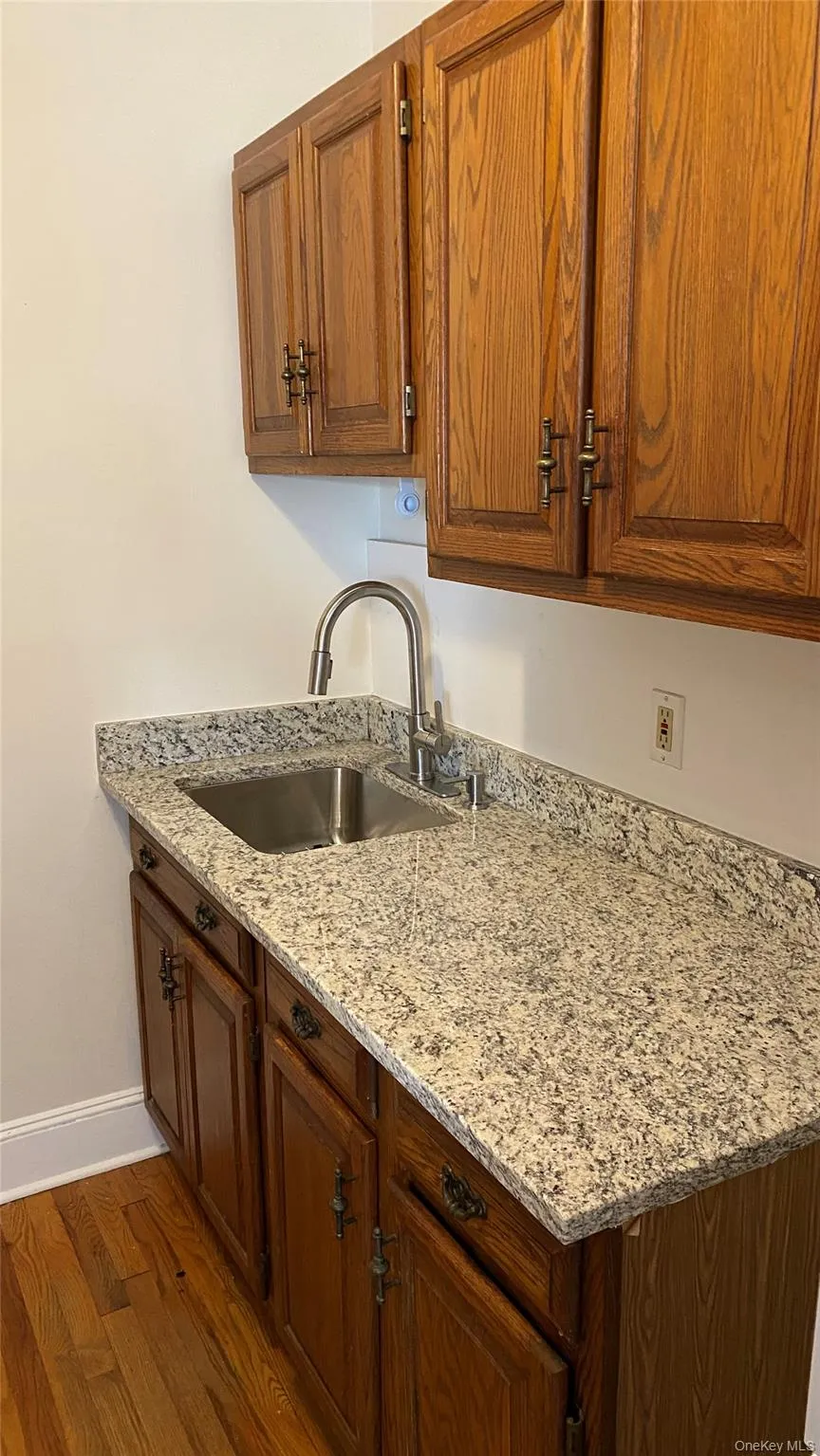 Wood-finish cabinetry with decorative hardware, solid surface countertop, stainless steel sink, and wood-finish flooring Wood-finish cabinetry with decorative hardware, solid surface countertop, stainless steel sink, and wood-finish flooring