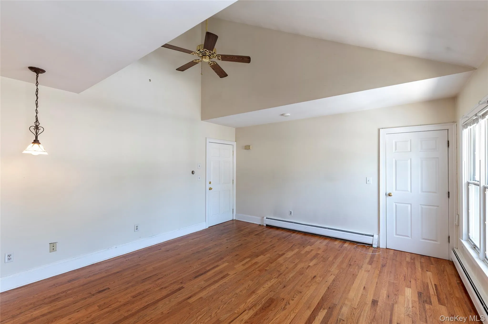 Unfurnished room featuring baseboard heating, high vaulted ceiling, light wood-style flooring, a ceiling fan, and plenty of natural light Unfurnished room featuring baseboard heating, high vaulted ceiling, light wood-style flooring, a ceiling fan, and plenty of natural light