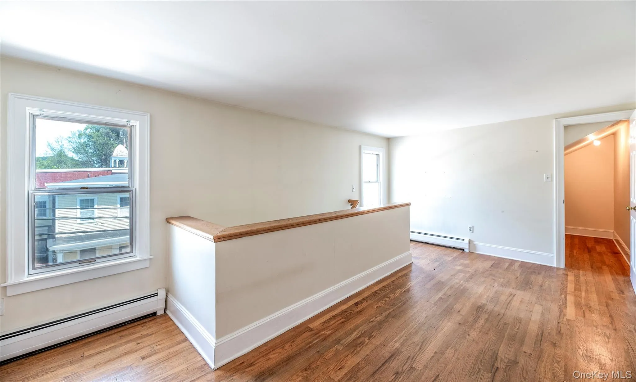 Empty room with baseboard heating, light wood-type flooring, and plenty of natural light Empty room with baseboard heating, light wood-type flooring, and plenty of natural light