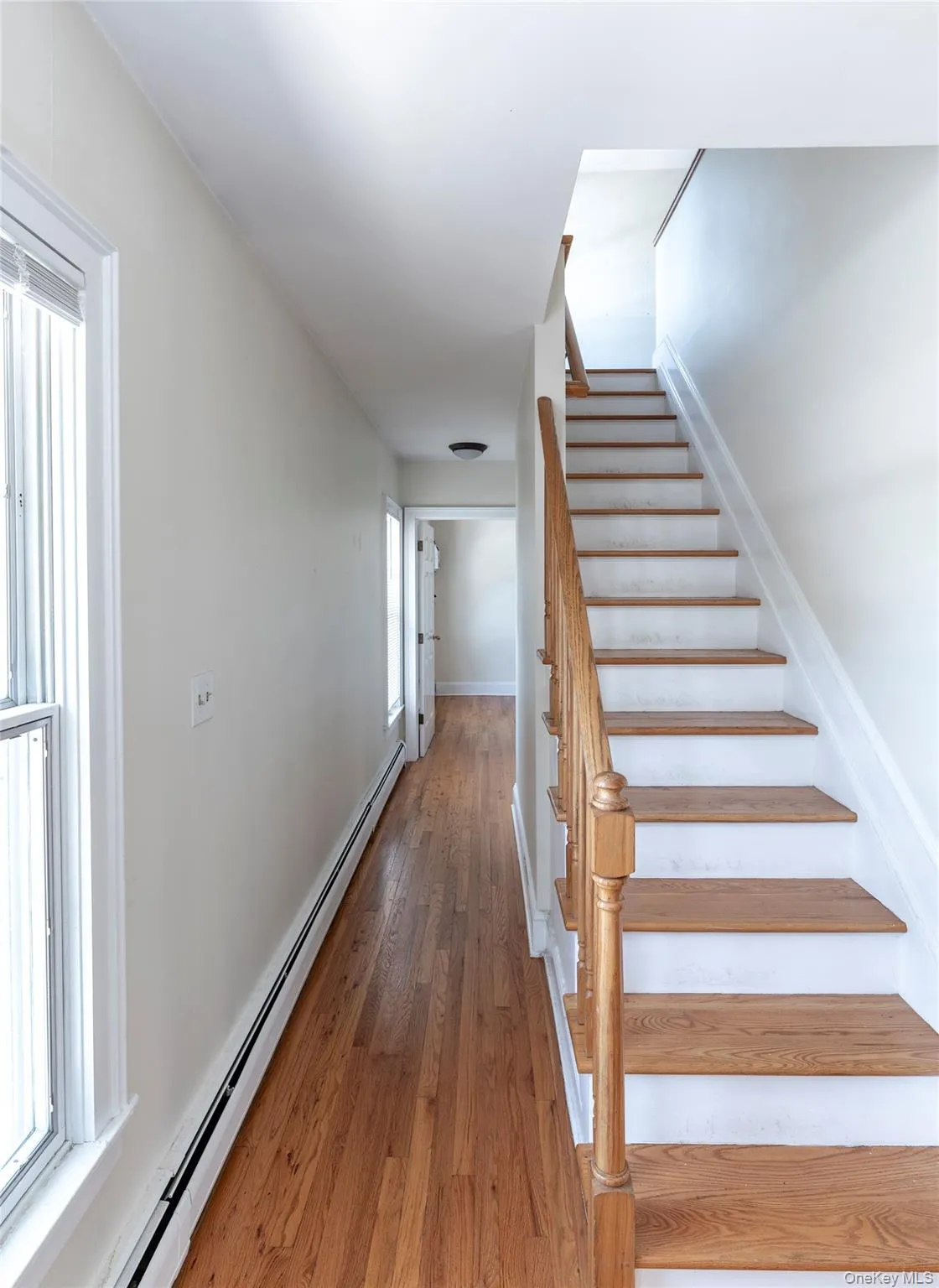Stairway featuring a baseboard heating unit, wood finished floors, and healthy amount of natural light Stairway featuring a baseboard heating unit, wood finished floors, and healthy amount of natural light