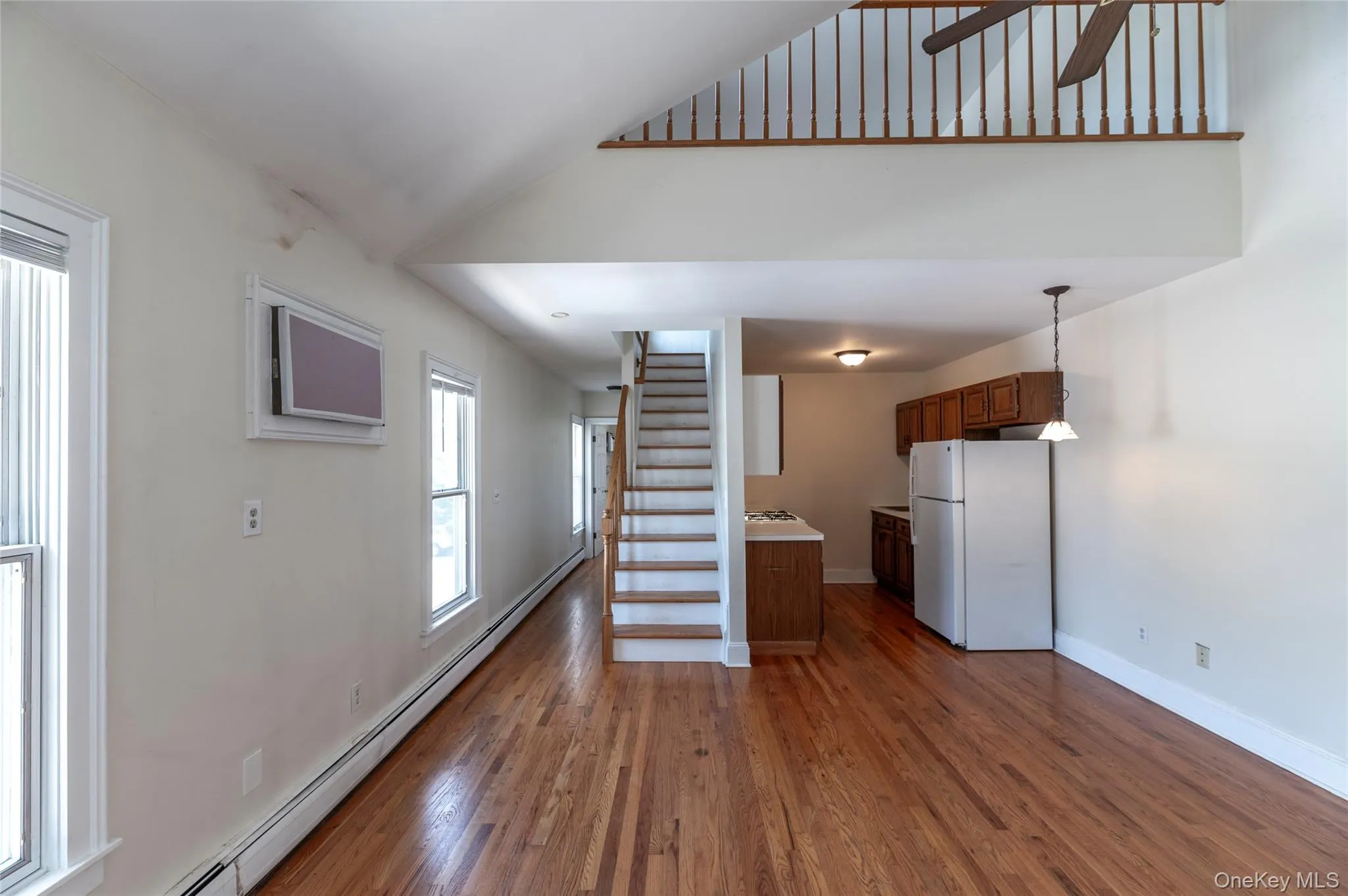 Unfurnished living room featuring baseboard heating, stairway, and wood finished floors Unfurnished living room featuring baseboard heating, stairway, and wood finished floors