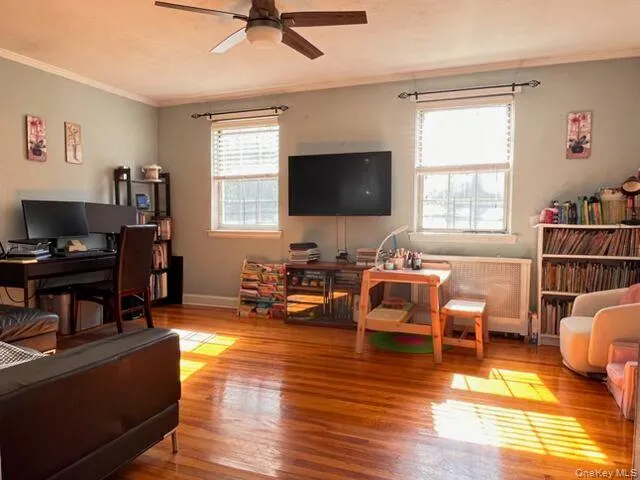 Hardwood flooring, two windows with blinds, crown molding, and a ceiling fan with integrated lighting Hardwood flooring, two windows with blinds, crown molding, and a ceiling fan with integrated lighting