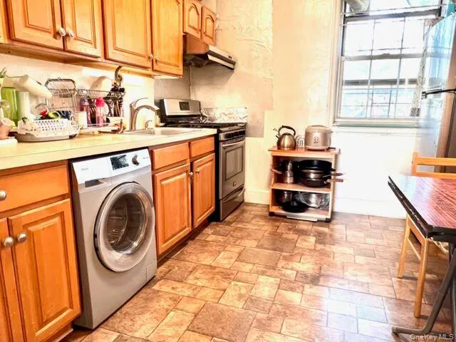 Kitchen with wood-finish cabinetry, light-toned countertops, and a built-in washer Kitchen with wood-finish cabinetry, light-toned countertops, and a built-in washer