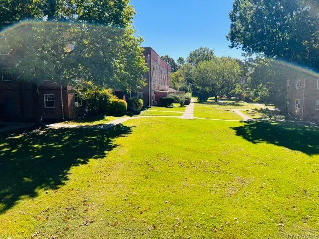 Expansive green space featuring mature trees and paved walkways, bordered by brick residential structures Expansive green space featuring mature trees and paved walkways, bordered by brick residential structures
