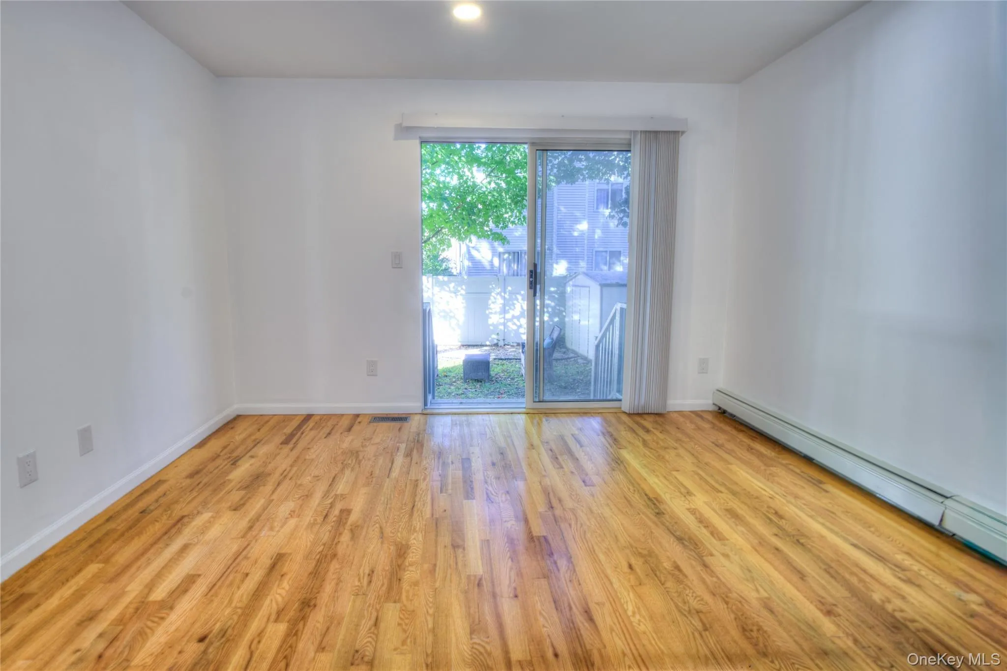 Hardwood flooring, sliding glass door, recessed lighting, white wall finishes, and a baseboard heating unit Hardwood flooring, sliding glass door, recessed lighting, white wall finishes, and a baseboard heating unit
