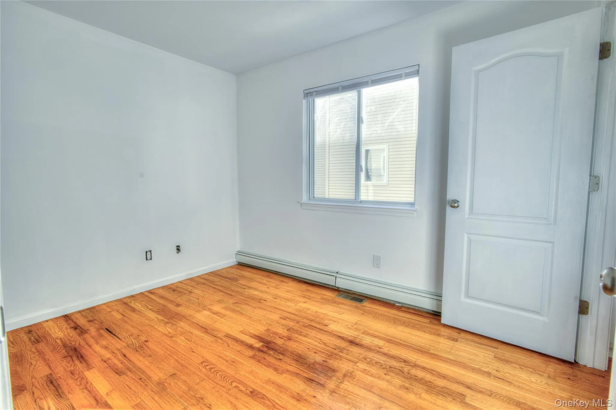 Wood-finish flooring, white paneled door, window with blinds, and white walls Wood-finish flooring, white paneled door, window with blinds, and white walls