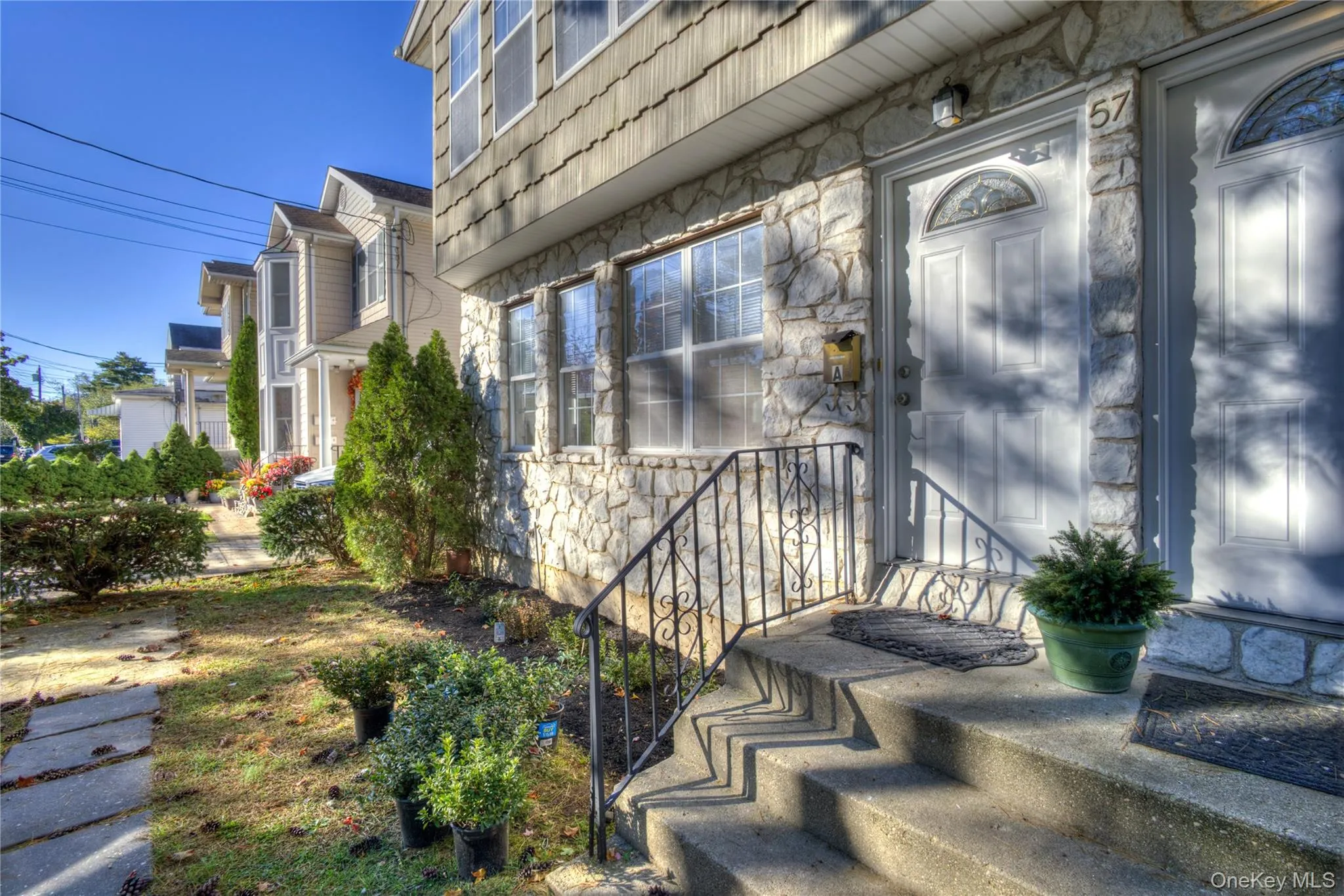 Stone veneer facade with wood-shake siding, concrete front steps with wrought iron railing, and a front entry door featuring a decorative arched window Stone veneer facade with wood-shake siding, concrete front steps with wrought iron railing, and a front entry door featuring a decorative arched window