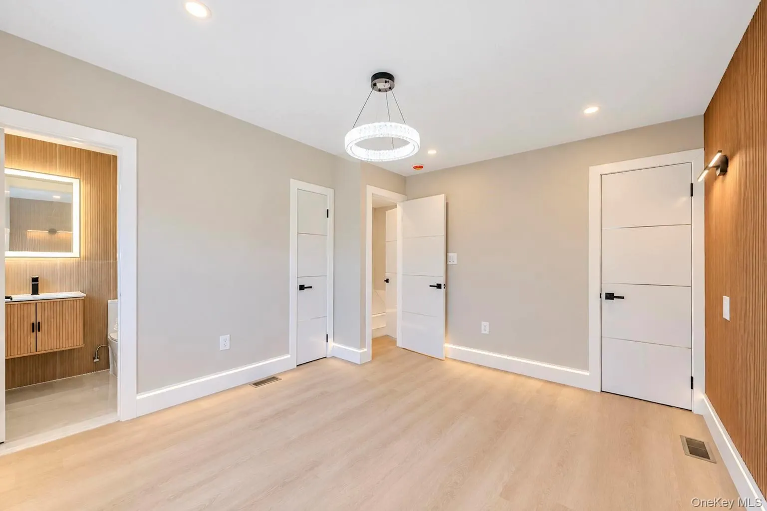 Recessed lighting, wood-finish flooring, a contemporary chandelier, a built-in floating vanity with an illuminated mirror, and modern interior doors with dark hardware. Recessed lighting, wood-finish flooring, a contemporary chandelier, a built-in floating vanity with an illuminated mirror, and modern interior doors with dark hardware.