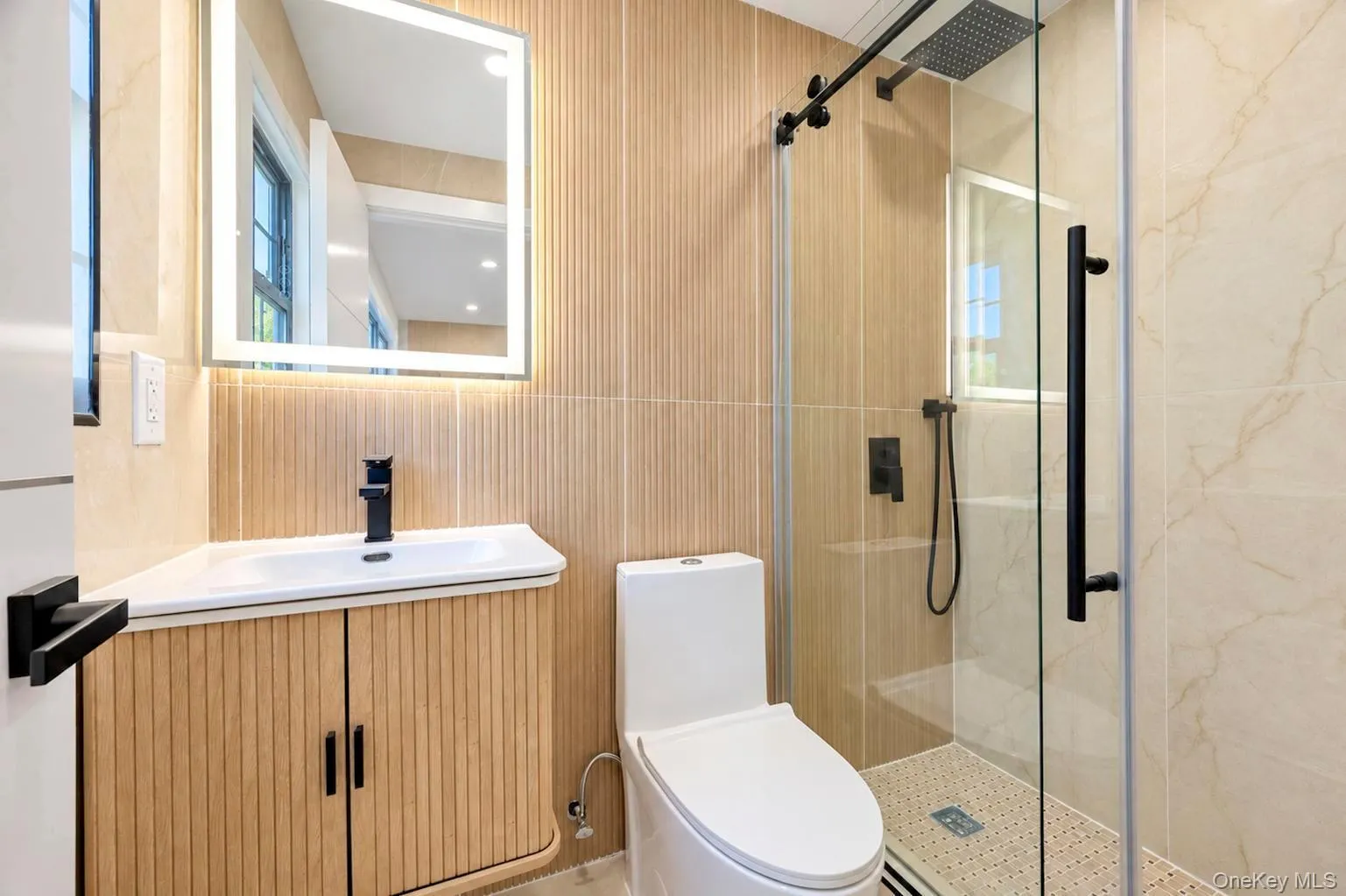 2nd bathroom located in the grand room Backlit mirror, wood-finish vanity, matte black fixtures, glass-enclosed shower, and tiled walls 2nd bathroom located in the grand room Backlit mirror, wood-finish vanity, matte black fixtures, glass-enclosed shower, and tiled walls