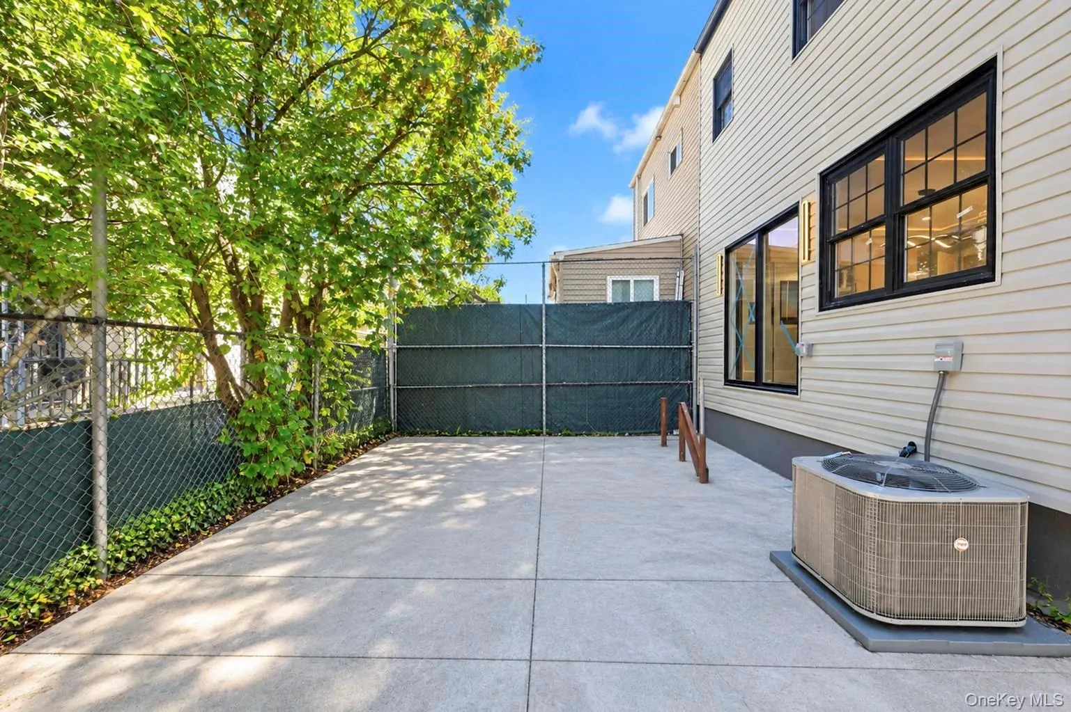 Paved patio area featuring a mature tree, secure chain-link fencing, and a siding exterior Paved patio area featuring a mature tree, secure chain-link fencing, and a siding exterior