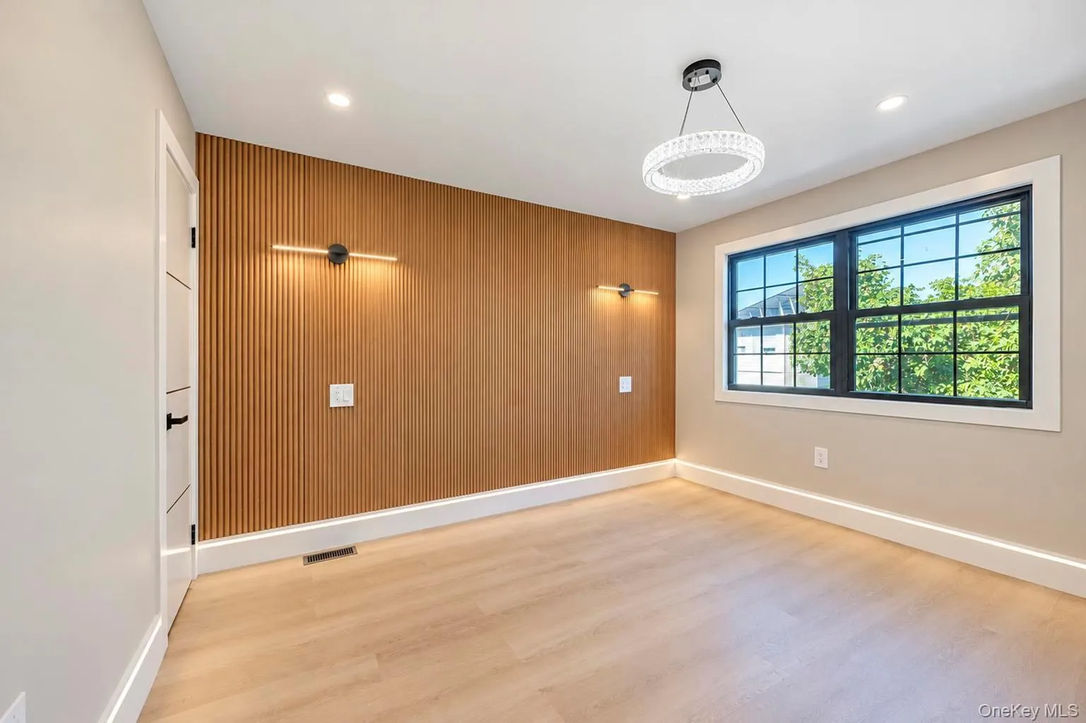 Wood-finished flooring throughout, featuring a slatted accent wall with integrated sconce lighting Wood-finished flooring throughout, featuring a slatted accent wall with integrated sconce lighting