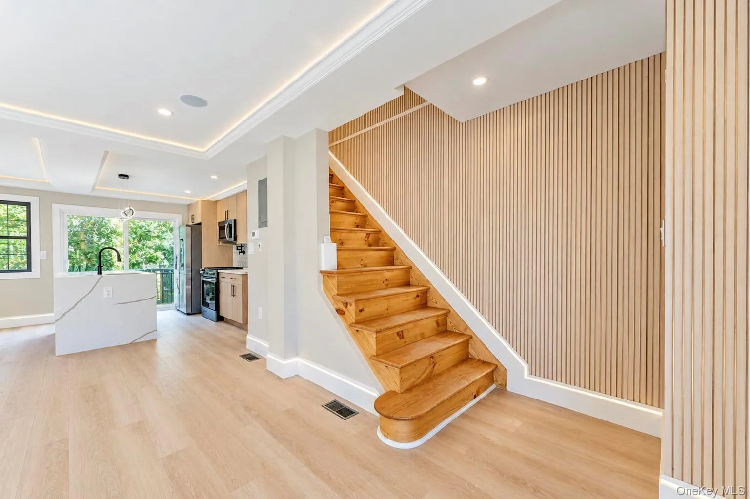Leading to 2nd FL Light wood-finish flooring, recessed ceiling lighting, kitchen island with waterfall countertop, wood slat accent wall, and wood staircase Leading to 2nd FL Light wood-finish flooring, recessed ceiling lighting, kitchen island with waterfall countertop, wood slat accent wall, and wood staircase