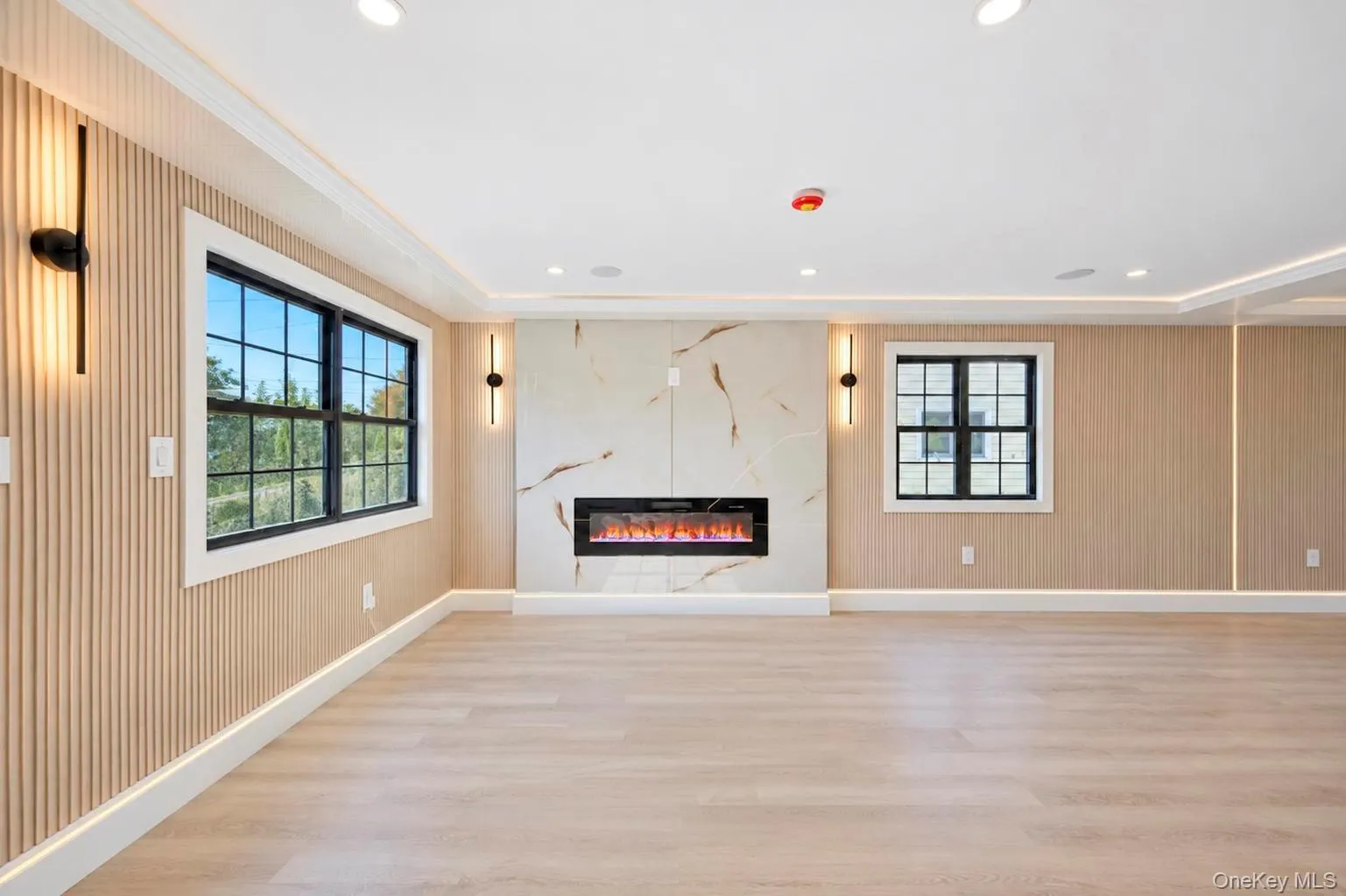 Wood-finish flooring with white baseboards, recessed lighting, and a built-in electric fireplace featuring a marble-patterned surround Wood-finish flooring with white baseboards, recessed lighting, and a built-in electric fireplace featuring a marble-patterned surround