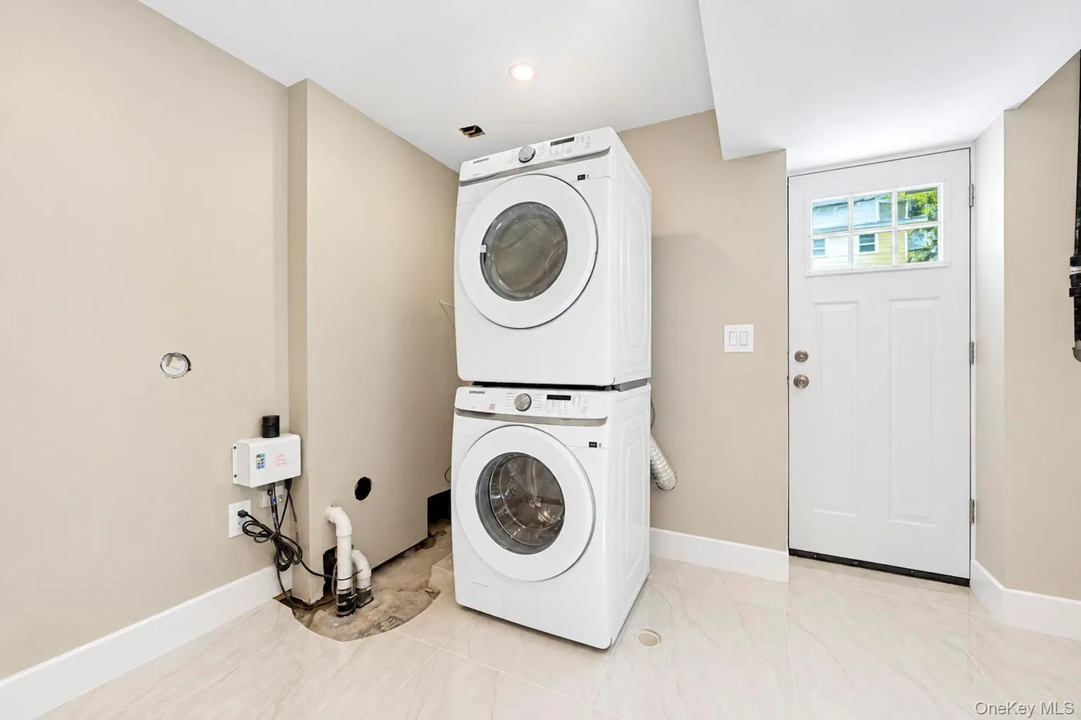 Stackable washer and dryer, recessed lighting, neutral paint, tiled flooring, and a white paneled door with window pane. Stackable washer and dryer, recessed lighting, neutral paint, tiled flooring, and a white paneled door with window pane.