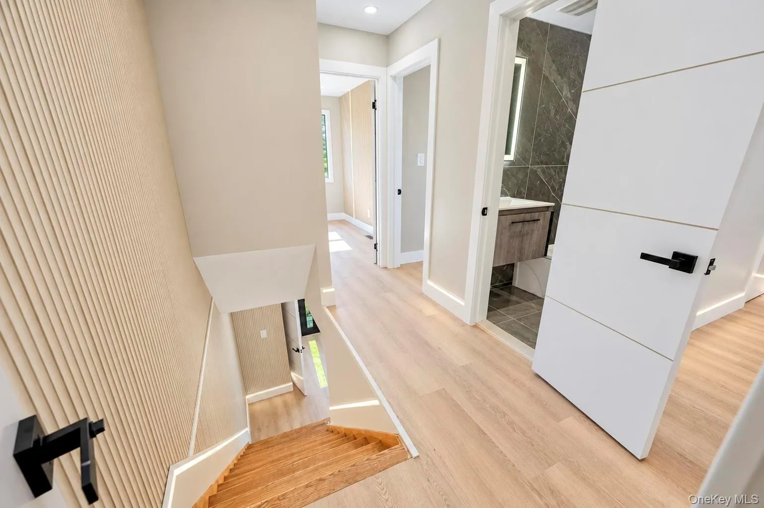 Light, wood-finish flooring throughout, modern white doors with black hardware, and a bathroom featuring a floating vanity with a vessel sink and a tiled accent wall Light, wood-finish flooring throughout, modern white doors with black hardware, and a bathroom featuring a floating vanity with a vessel sink and a tiled accent wall