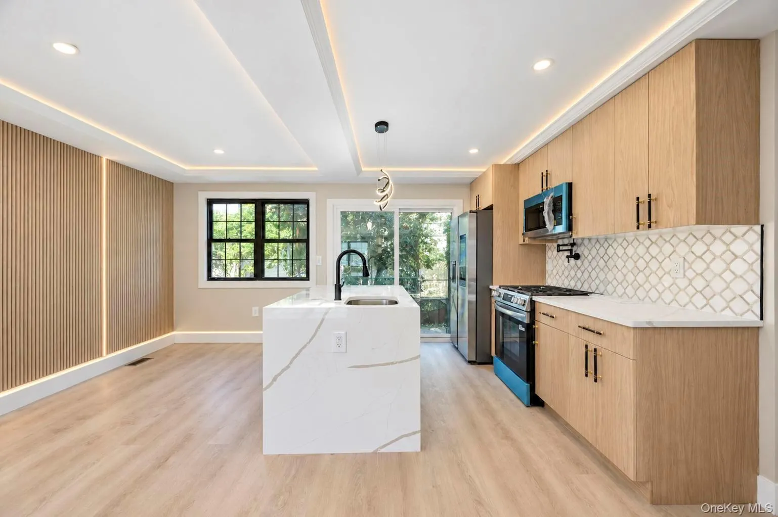 Modern kitchen featuring wood-finish cabinetry, a patterned tile backsplash, stainless steel appliances, and a waterfall island with a sink. Modern kitchen featuring wood-finish cabinetry, a patterned tile backsplash, stainless steel appliances, and a waterfall island with a sink.