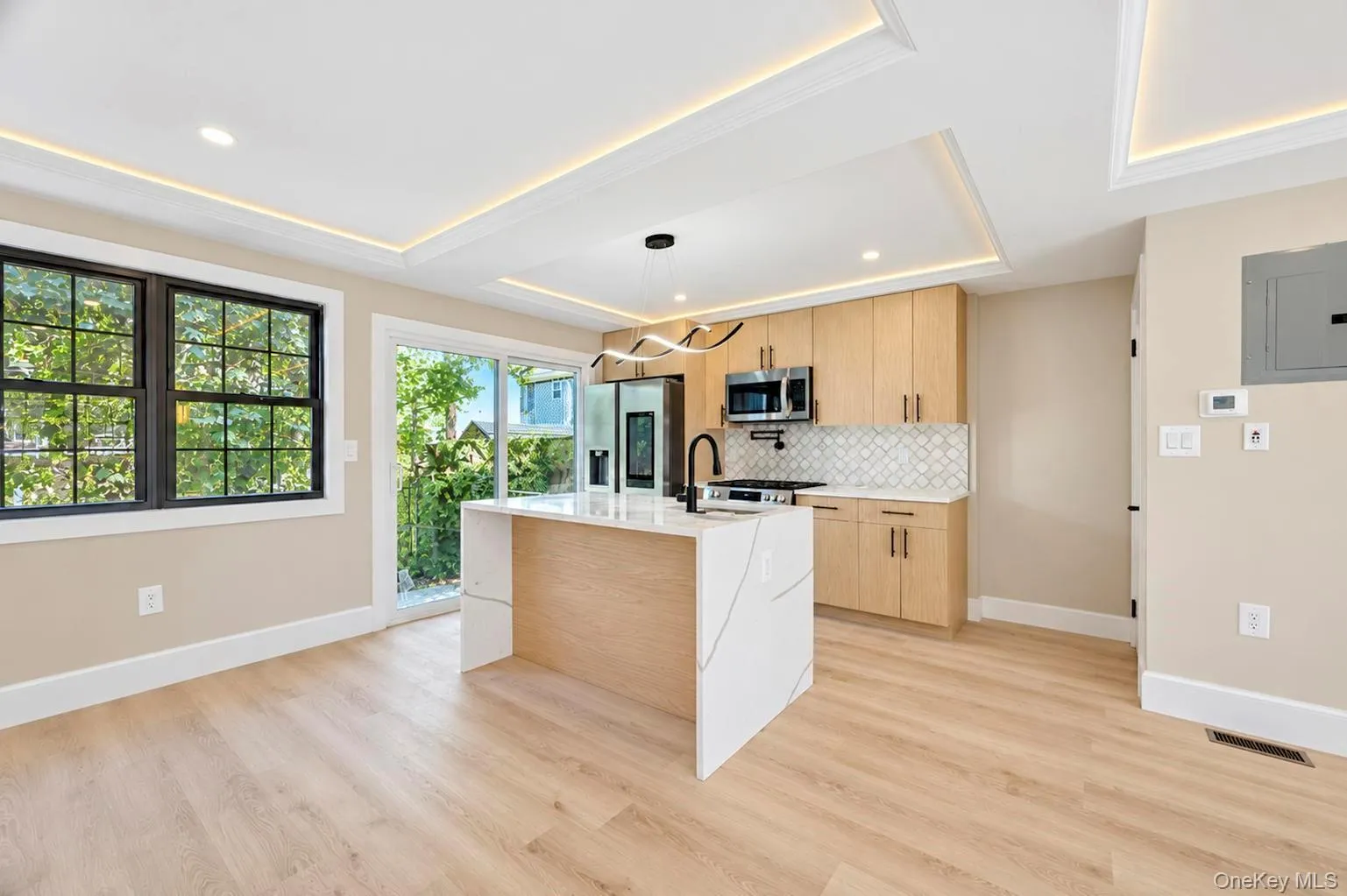 Kitchen featuring wood-finish cabinetry, a central island with a waterfall countertop, and a patterned tile backsplash. Kitchen featuring wood-finish cabinetry, a central island with a waterfall countertop, and a patterned tile backsplash.