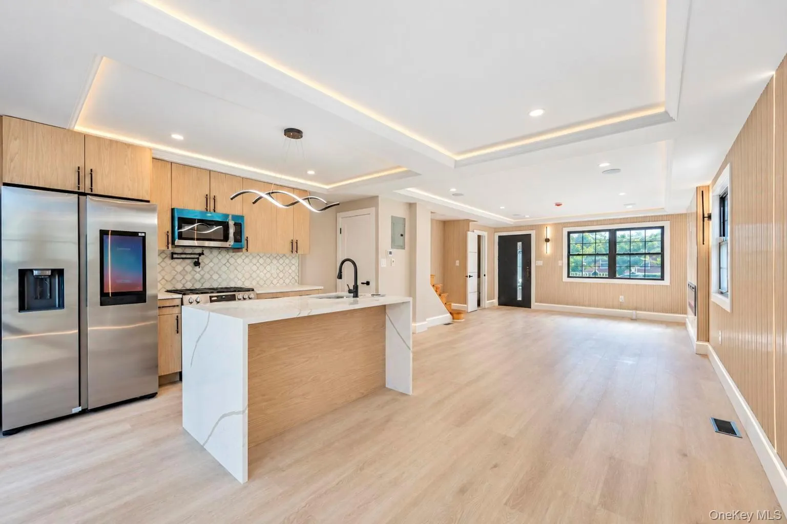 Kitchen and living area featuring a waterfall island, stainless steel refrigerator, light wood-finish flooring, recessed lighting, and a modern chandelier Kitchen and living area featuring a waterfall island, stainless steel refrigerator, light wood-finish flooring, recessed lighting, and a modern chandelier
