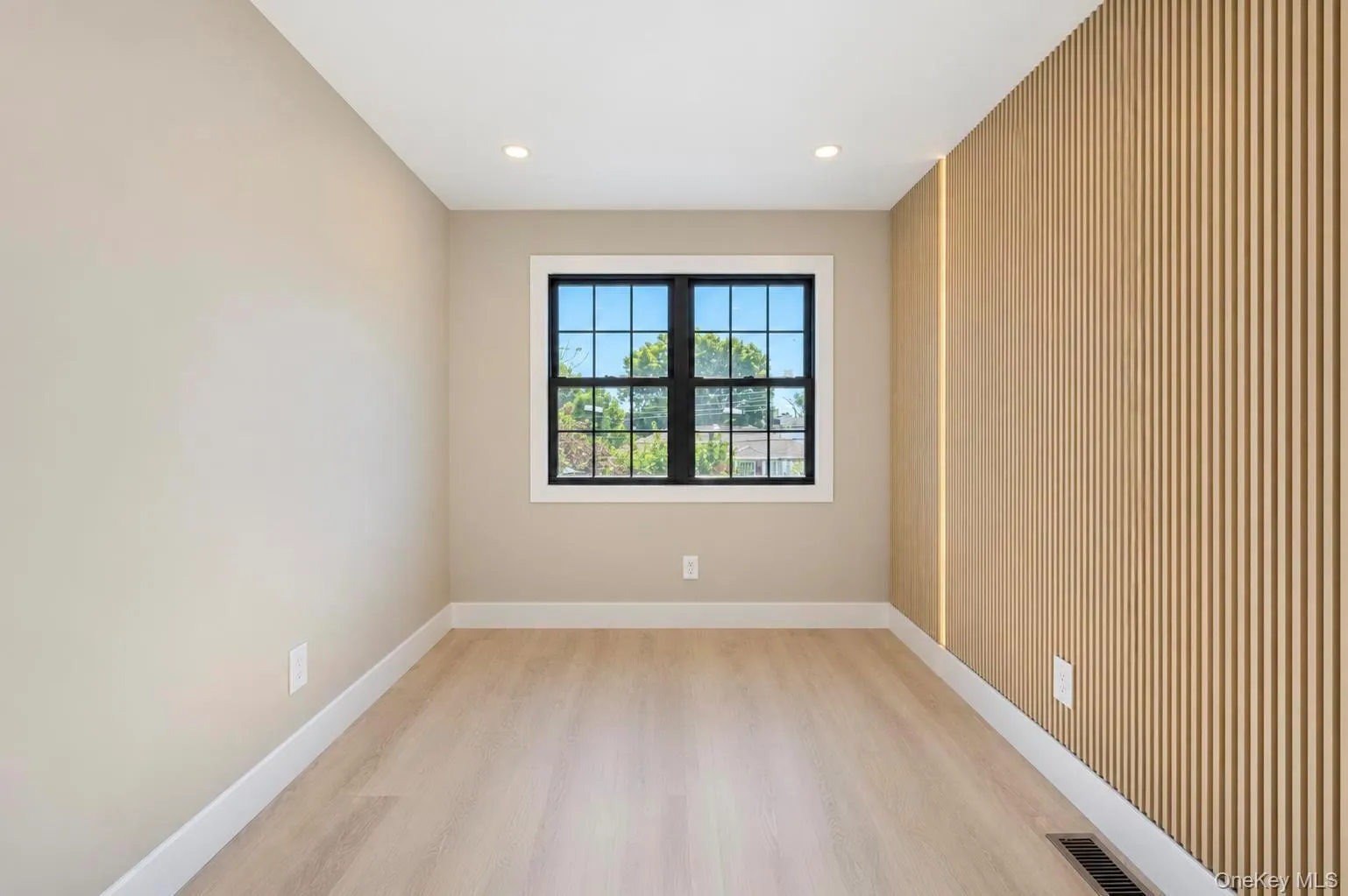Light wood-finish flooring, recessed ceiling lighting, a black-framed. window with grid, and a feature wall with vertical wood paneling and integrated vertical lighting Light wood-finish flooring, recessed ceiling lighting, a black-framed. window with grid, and a feature wall with vertical wood paneling and integrated vertical lighting