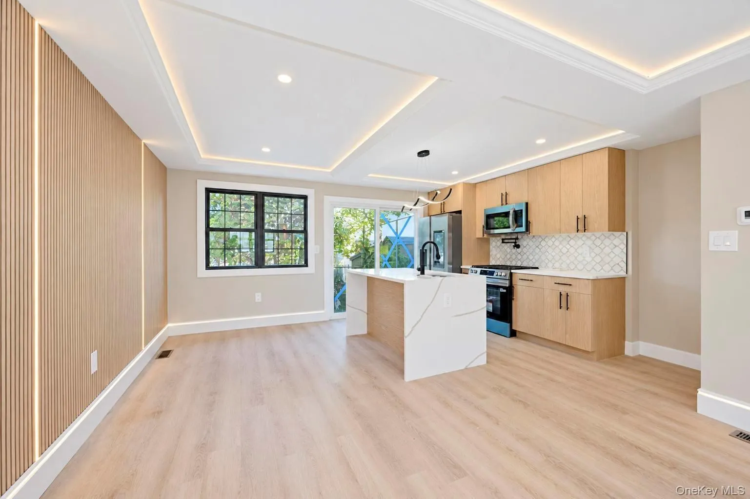 Recessed ceiling with perimeter lighting, wood-finish flooring, kitchen island with integrated sink, light wood cabinetry, and a black-framed window Recessed ceiling with perimeter lighting, wood-finish flooring, kitchen island with integrated sink, light wood cabinetry, and a black-framed window