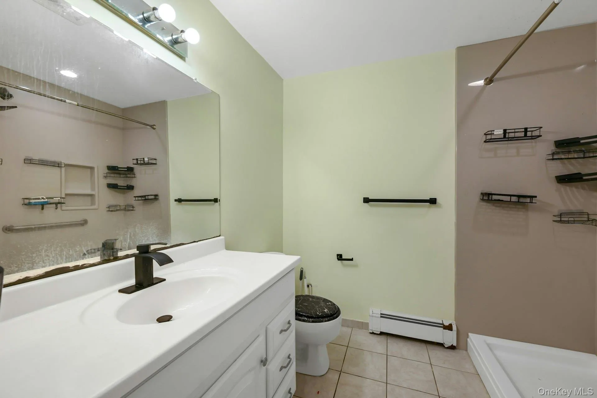 Bathroom featuring a shower, light tile patterned floors, vanity, and baseboard heating Bathroom featuring a shower, light tile patterned floors, vanity, and baseboard heating