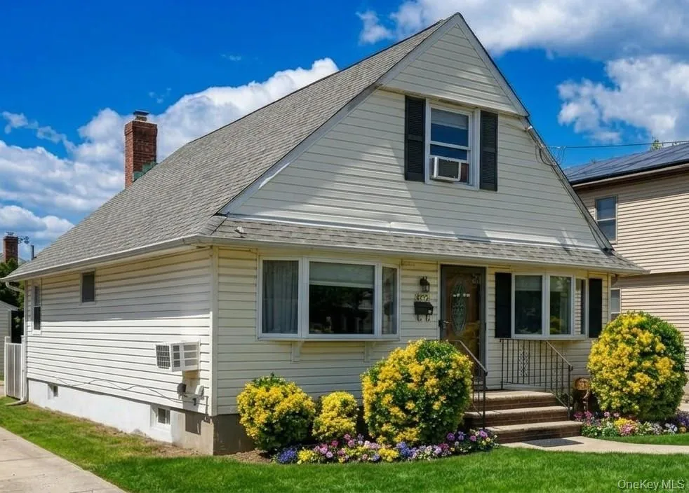 Featuring cream-colored siding, a steeply pitched roof, bay windows, and a brick chimney Featuring cream-colored siding, a steeply pitched roof, bay windows, and a brick chimney