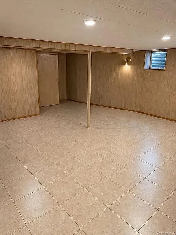 Finished lower-level space featuring tile flooring, vertical wood-panel wall finishing, recessed ceiling lighting, and a structural support column Finished lower-level space featuring tile flooring, vertical wood-panel wall finishing, recessed ceiling lighting, and a structural support column