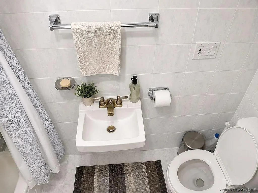 Wall-mounted porcelain sink featuring a metallic dual-handle faucet, surrounded by floor-to-ceiling white ceramic wall tile and chrome-finish bathroom hardware Wall-mounted porcelain sink featuring a metallic dual-handle faucet, surrounded by floor-to-ceiling white ceramic wall tile and chrome-finish bathroom hardware
