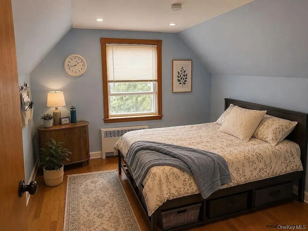 Bedroom featuring wood-finish flooring, sloped ceilings, and a window framed by wood trim Bedroom featuring wood-finish flooring, sloped ceilings, and a window framed by wood trim