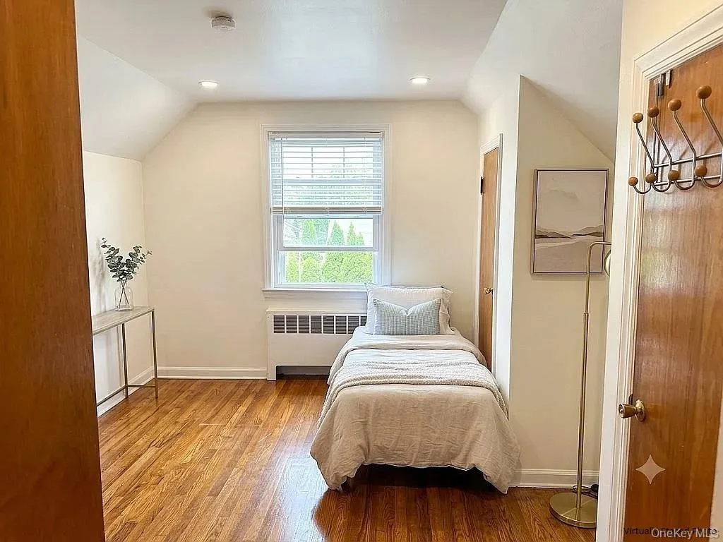 Room with hardwood flooring, recessed ceiling lighting, a window with horizontal blinds, and a custom-fitted radiator cover Room with hardwood flooring, recessed ceiling lighting, a window with horizontal blinds, and a custom-fitted radiator cover