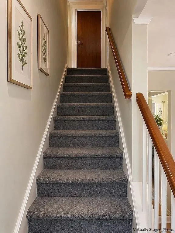 Staircase featuring charcoal carpeted treads, wood handrails, white balusters, and neutral wall tones Staircase featuring charcoal carpeted treads, wood handrails, white balusters, and neutral wall tones
