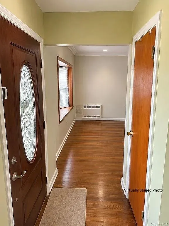 Entryway featuring a solid wood door with oval decorative glass insert, wood-finish flooring, a wood-trimmed bay window, and a built-in wall HVAC unit Entryway featuring a solid wood door with oval decorative glass insert, wood-finish flooring, a wood-trimmed bay window, and a built-in wall HVAC unit