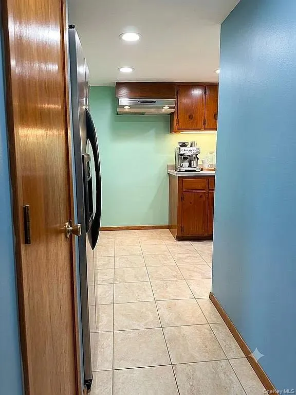 Kitchen featuring wood cabinetry, stainless steel range hood, ceramic tile flooring, and recessed ceiling lighting Kitchen featuring wood cabinetry, stainless steel range hood, ceramic tile flooring, and recessed ceiling lighting