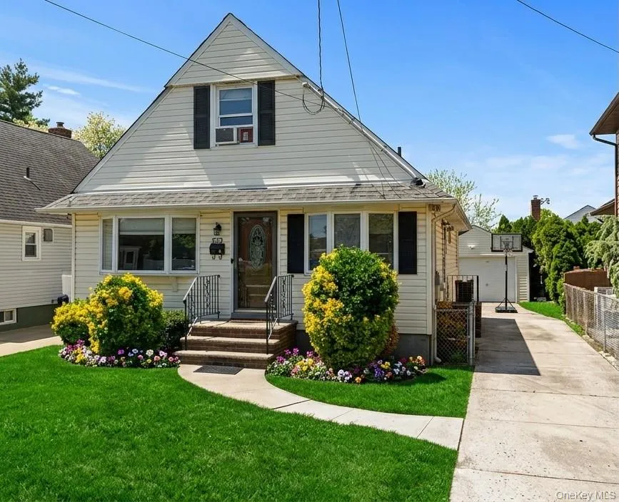 Featuring light-toned vinyl siding, decorative shutters, a concrete driveway, detached garage, and front entryway with stone steps and iron railings Featuring light-toned vinyl siding, decorative shutters, a concrete driveway, detached garage, and front entryway with stone steps and iron railings
