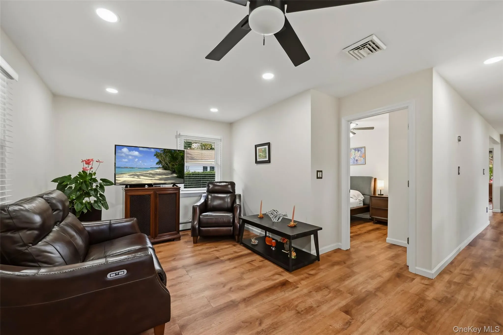 Spacious living room showcasing warm wood-finish flooring, recessed ceiling lighting, and a ceiling fan with integrated light fixture Spacious living room showcasing warm wood-finish flooring, recessed ceiling lighting, and a ceiling fan with integrated light fixture